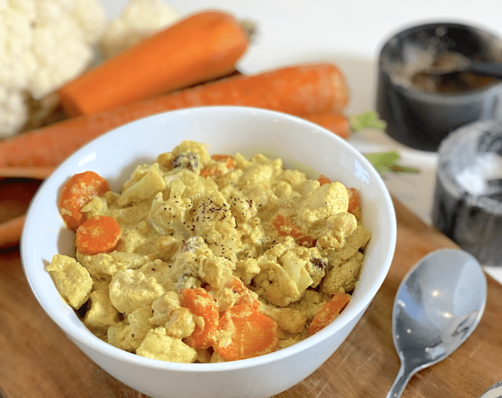 A bowl of Chicken Chickpea Cauliflower Curry with blurred carrots and cauliflower as background