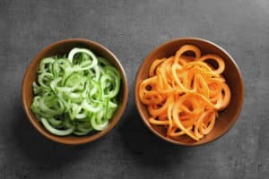 Bowls with cucumber and carrot spaghetti on grey background