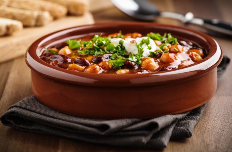 Hot stew with chick peas beans, soy, and chili peppers in a brown dish on a wooden table