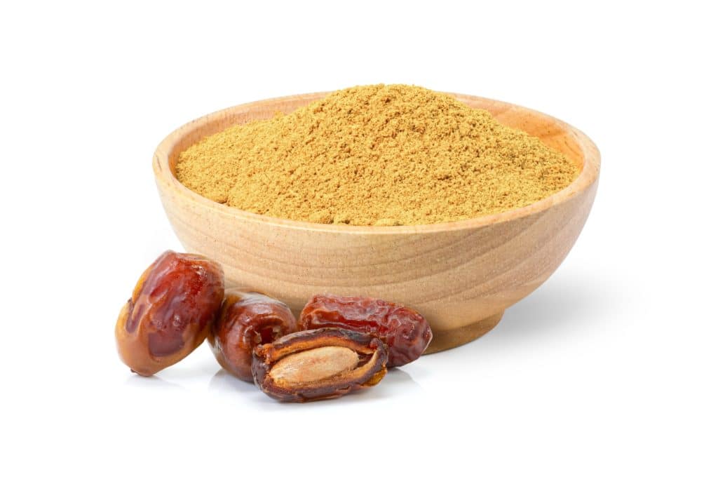 Date fruit powder in wooden bowl with dry dates fruits isolated on white background. Healthiest Sugar Substitute