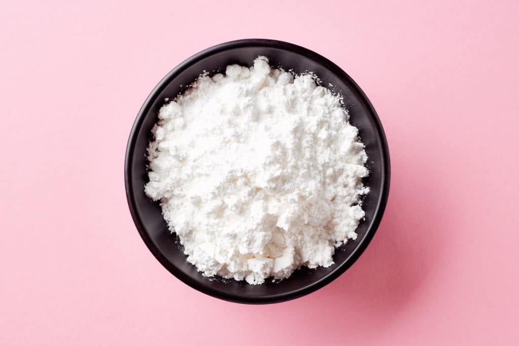 Bowl of powder allulose on pink background. Healthy sugar substitute