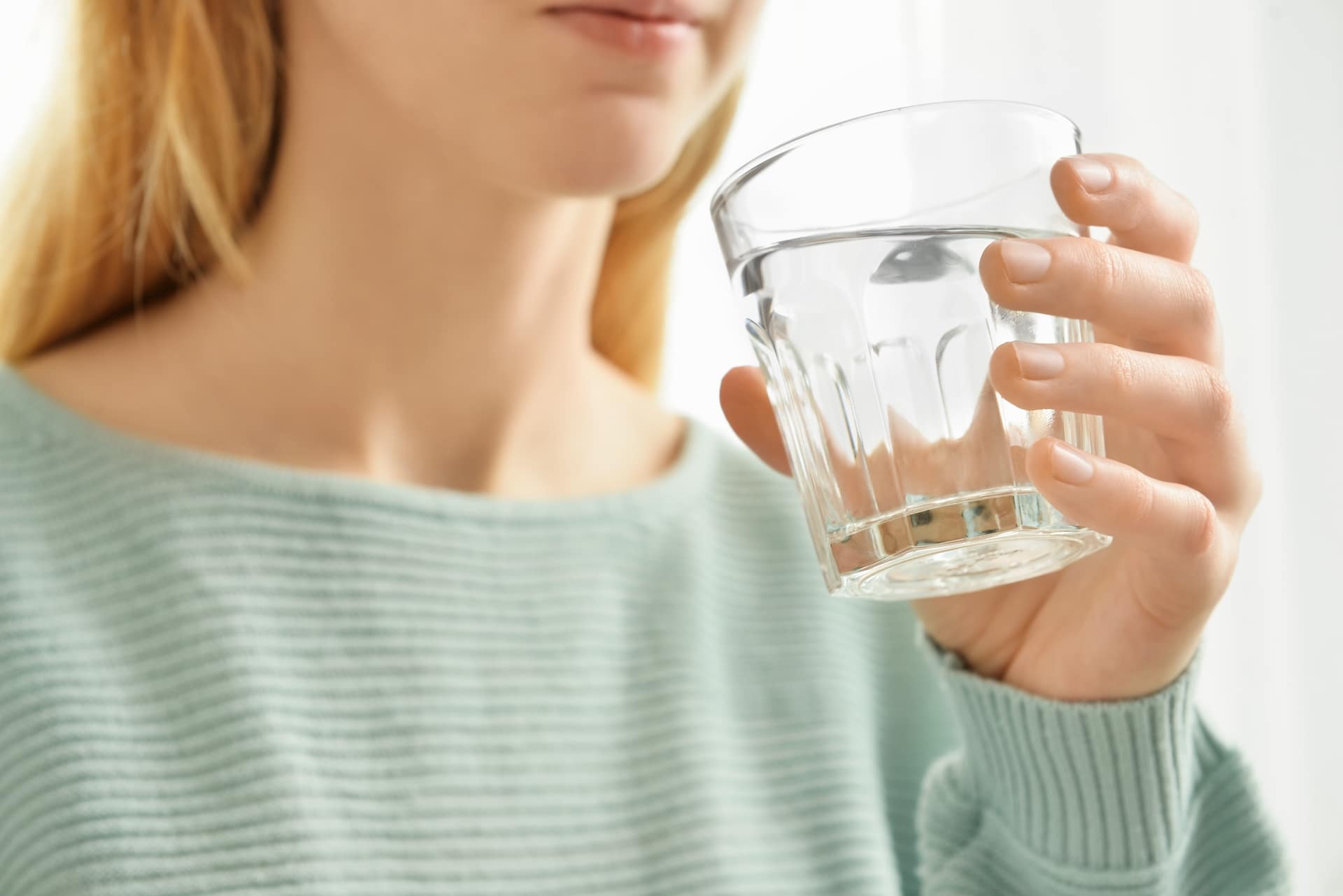 Woman in mint green sweater drinking fresh water in a glass.