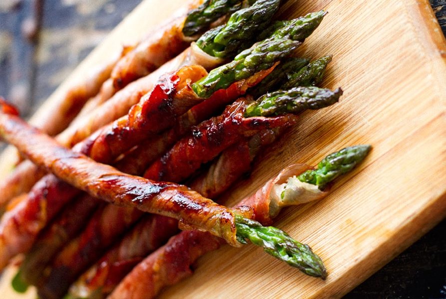 prosciutto wrapped asparagus on wooden chopping board