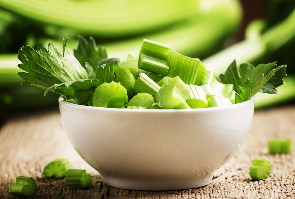 Chopped celery in a white bowl on a wooden background