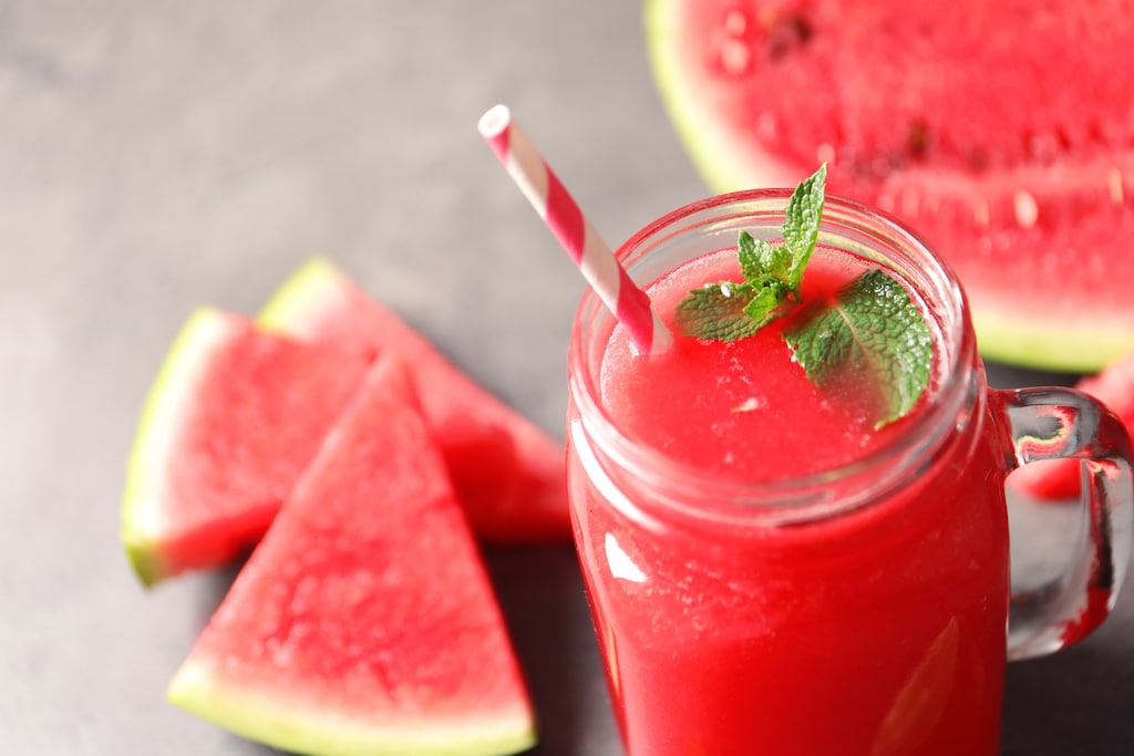 Summer watermelon drink with mint in mason jar and sliced fruit on table
