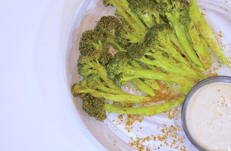 Broccoli Sticks on a white plate with sprinkled wheat germ and yogurt dip