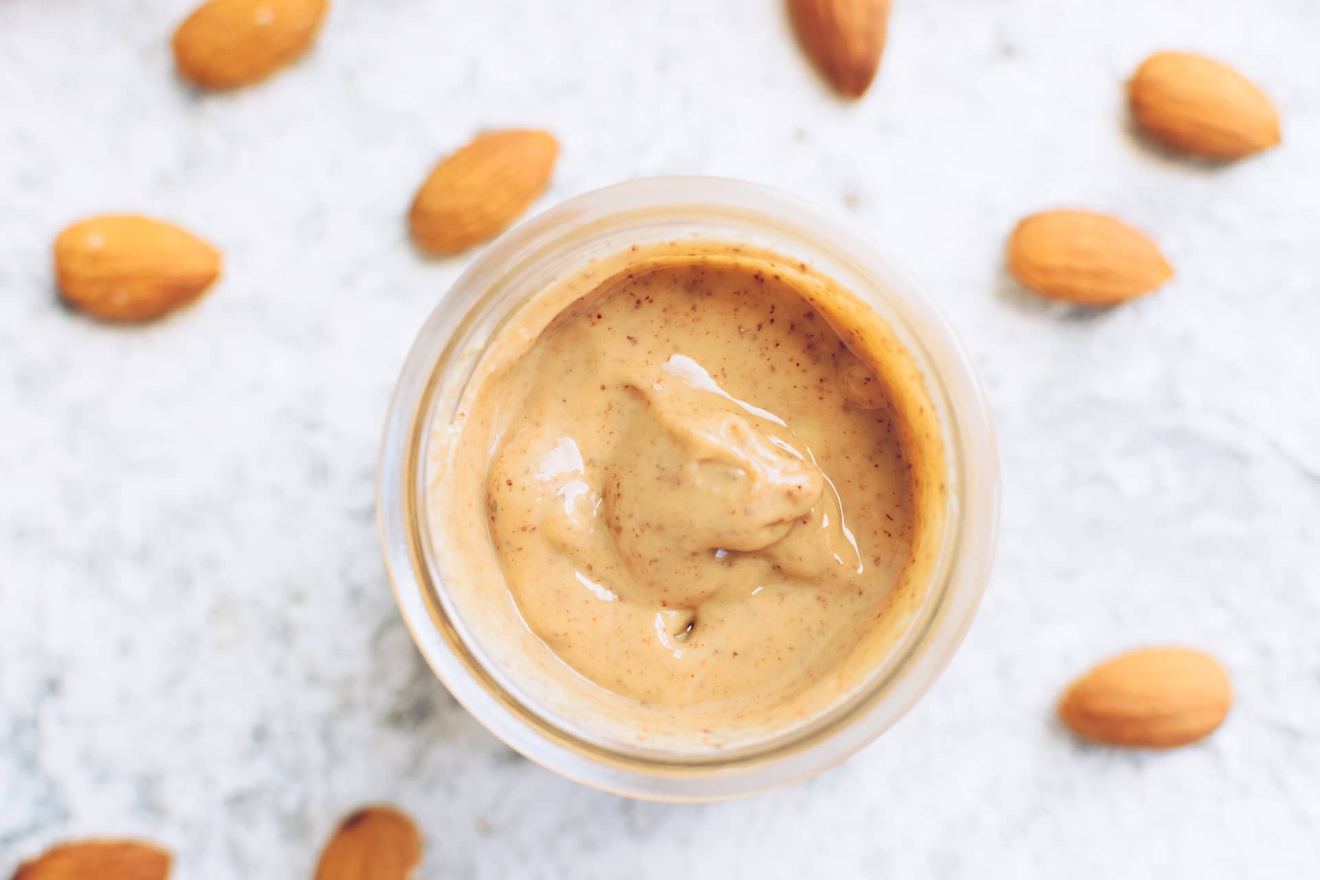 Almond nut butter in glass jar. Homemade raw organic almond nuts paste on grey background. Healthy natural food.