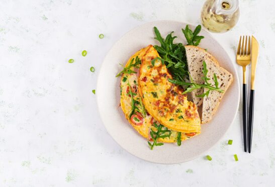 Omelette with tomatoes, ham, cheese and green herbs on plate.