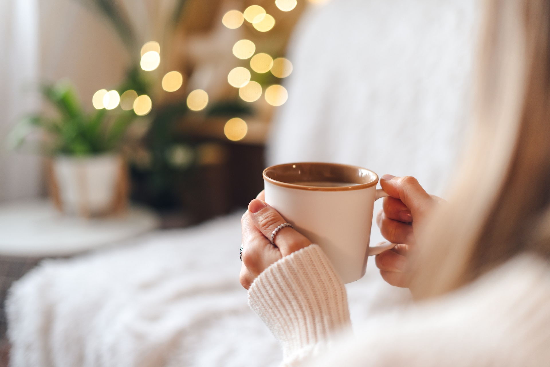 Woman's hands in sweater holding cup of hot drink coffee indoors.