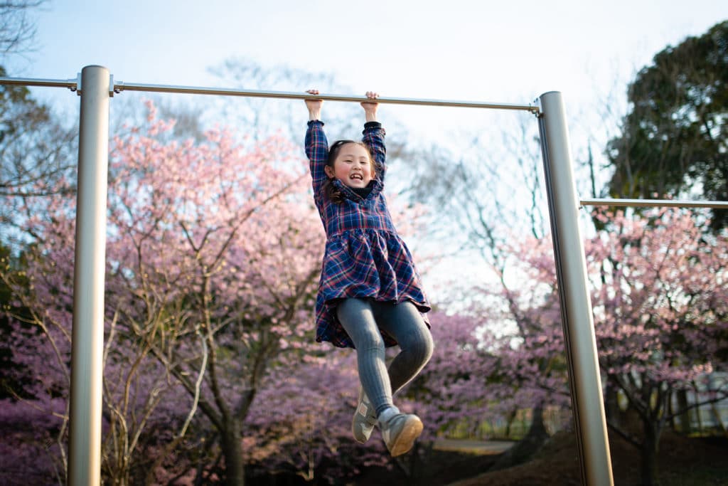 Girl playing a horizontal bar in a park where cherry blossoms bloom