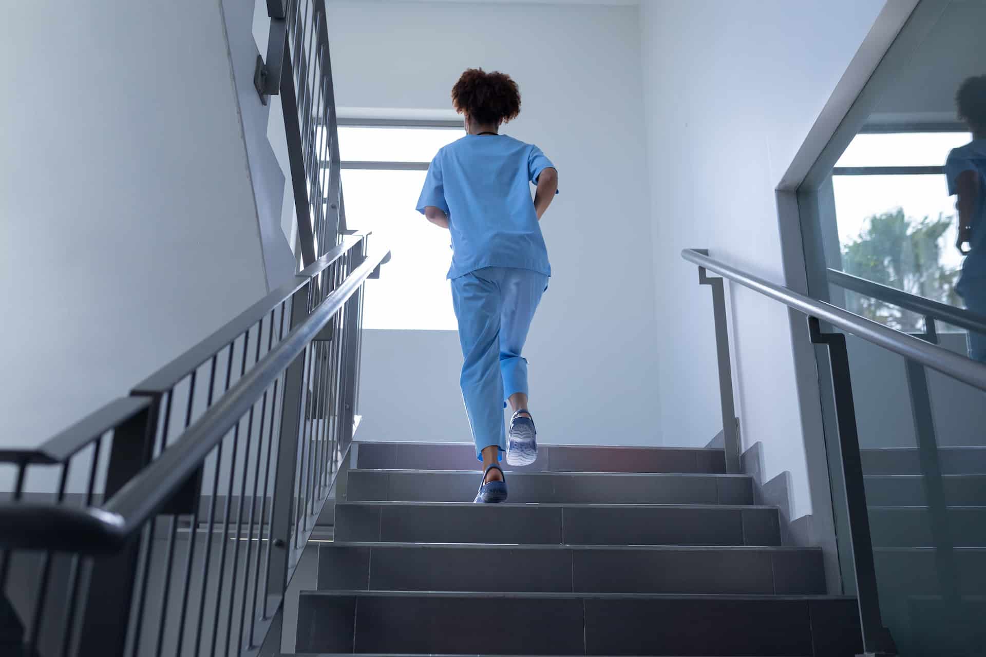 Rear view of young female doctor wearing scrubs running up stairs in hospital