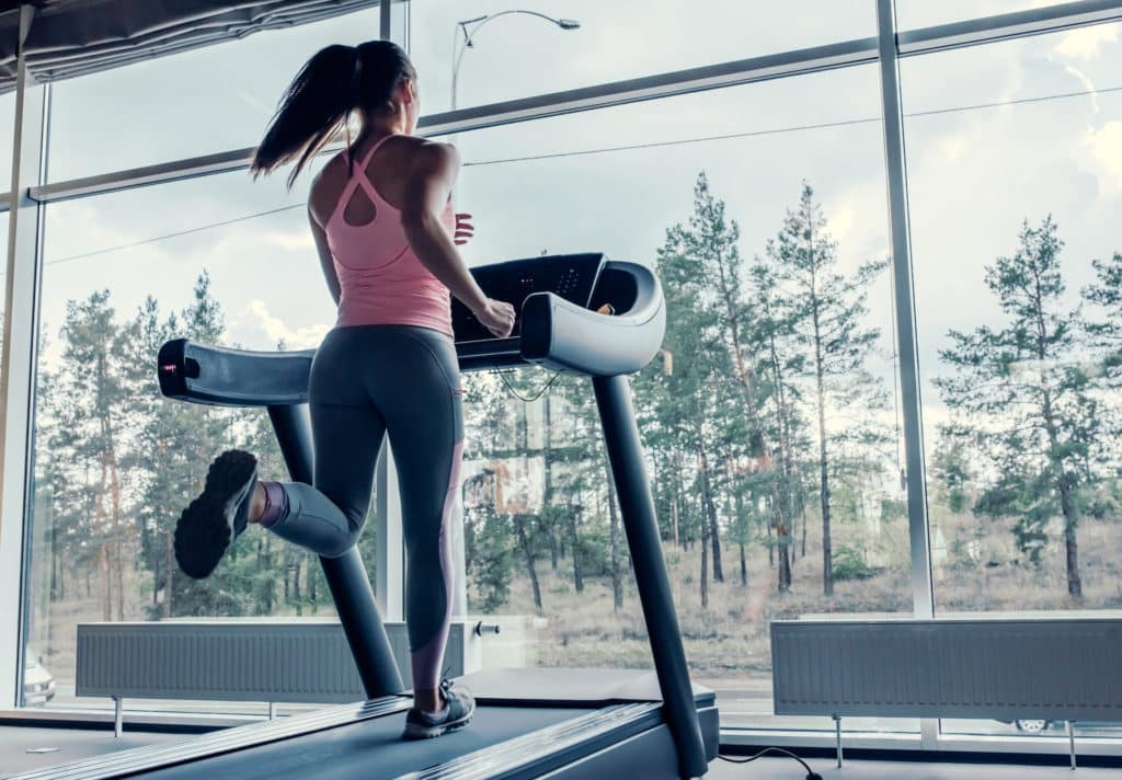 Attractive young sports woman is working out in gym. Doing short cardio workout on treadmill. Running on treadmill.